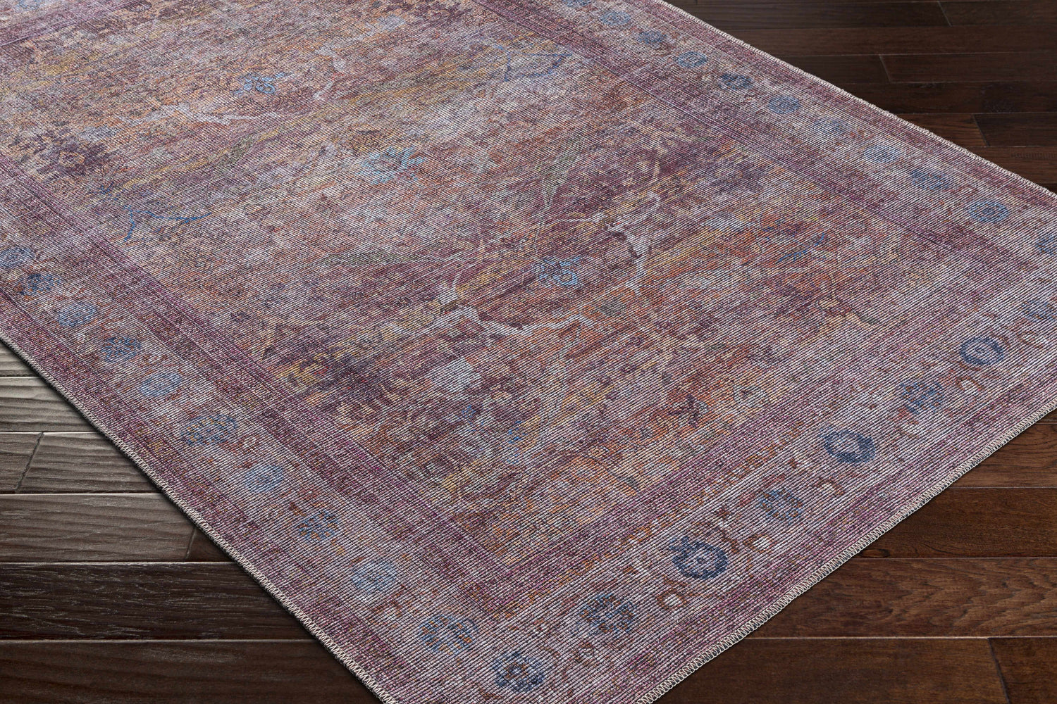 Close-up of the Alcoy Washable Area Rug. Features a traditional, oriental design in dark purple, brown, and pale pink tones. Corner