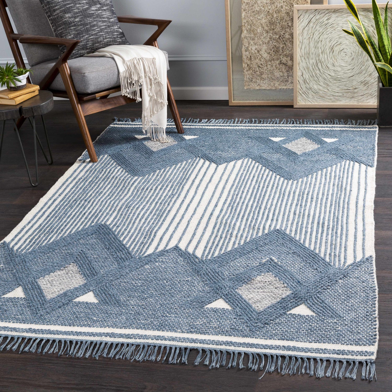 Living room scene with Aldbourne Blue Tassel Flatweave Wool Rug, gray chair, wood floors, and neutral art. Roomscene-Rectangle