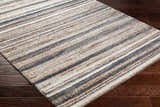 Close-up of the Alejo Area Rug on dark wood floors. Features a contemporary stripe pattern in clay, dusty sage, off-white, and walnut. Corner