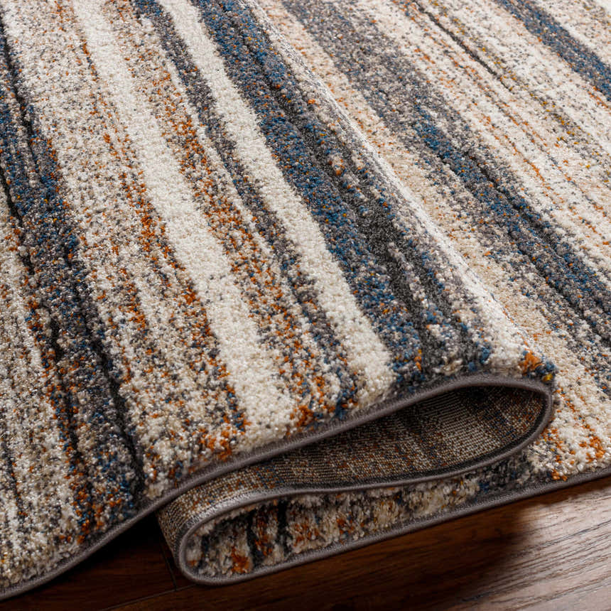 Close-up of the Alejo Area Rug showing its geometric pattern in clay, dusty sage, off white, and walnut hues. Fold