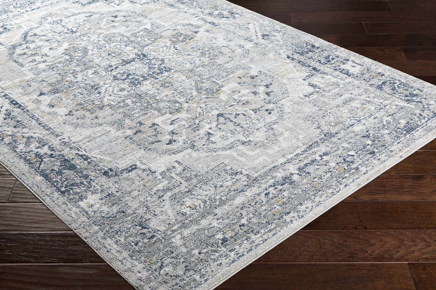 Close-up of the Allerton Area Rug showing its beige, charcoal, and dark blue traditional pattern on dark wood flooring. Corner