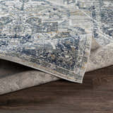 Close-up of the Allerton Area Rug showing its beige, charcoal, dark blue, and gray traditional pattern and machine-woven texture. Fold