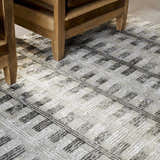 Close-up of the Aldis Grey Plush Textured Washable Rug featuring a geometric pattern and neutral colors under a wood chair. Styleshot
