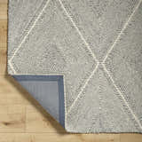 Close-up of the hand-tufted Amari Area Rug. Light gray and natural gray wool rug with a geometric diamond pattern. Fold