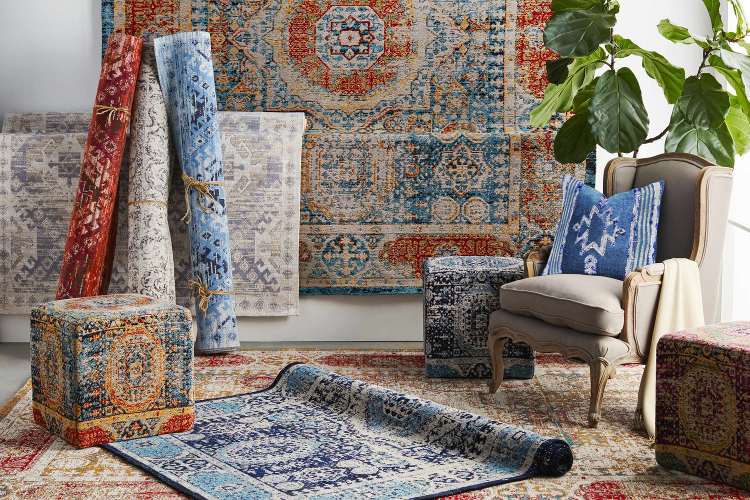 Styled room scene with Wrangell Blue/Red Damask Carpet, rolled rugs, patterned ottomans, and a gray chair with a blue pillow. Styleshot