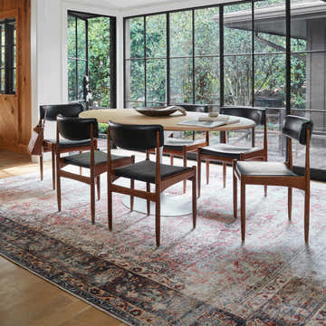 Dining room with oval table and black chairs on Rust Anahawan Distressed Washable Area Rug. Large windows view lush greenery. Roomscene-Rectangle