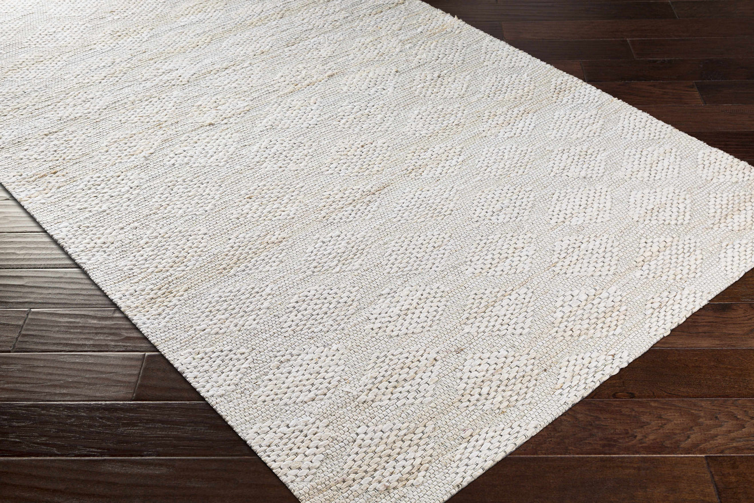 Close-up of the beige hand-woven Angaston Jute Rug showing texture and pattern on dark wood floors. Contemporary style. Corner