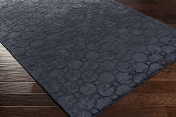 Close-up of the Ink Blue Annan Area Rug on dark wood floors, featuring a contemporary geometric circle pattern. Corner