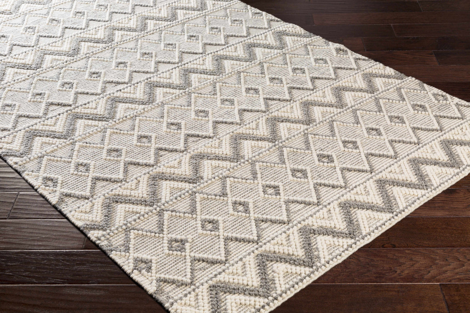 Close-up of the hand woven Whittington Gray&Cream Wool Rug showing its geometric pattern and textured wool on wood floor. Corner