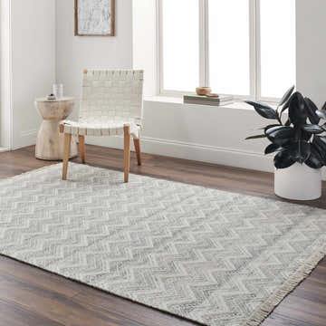 Living room scene with a hand-woven Aqeel Area Rug in gray and brown chevron pattern, paired with a woven chair and wood accents. Roomscene-Rectangle