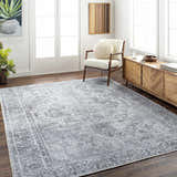 Living room scene with the gray Aquino Washable Area Rug, wood floors, chair, and console table. Bright, airy feel. Roomscene-Rectangle