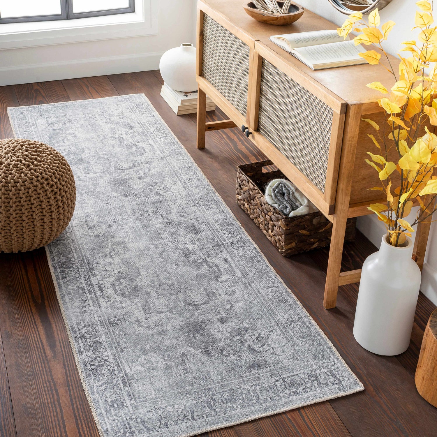Entryway scene with a gray Aquino Washable Area Rug runner, wood console table, woven pouf, and dark wood floors. Roomscene-Runner