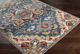 Close-up of the Argyle Area Rug, a machine-woven rug with a traditional design in brick red, navy, and tan colors. Corner