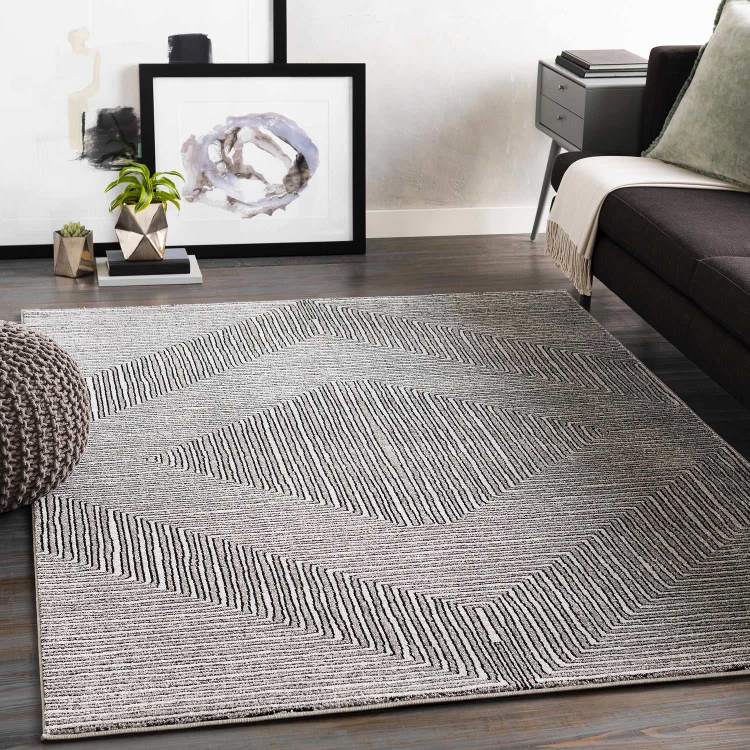 Living room scene with a gray sofa, pouf, and Artois Area Rug in a geometric black and cream pattern. Roomscene-Rectangle