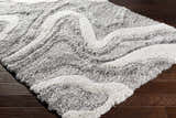 Close-up of the plush Asfordby Gray Canyon Rug showing its charcoal, gray, and off-white wavy pattern and soft texture. Corner