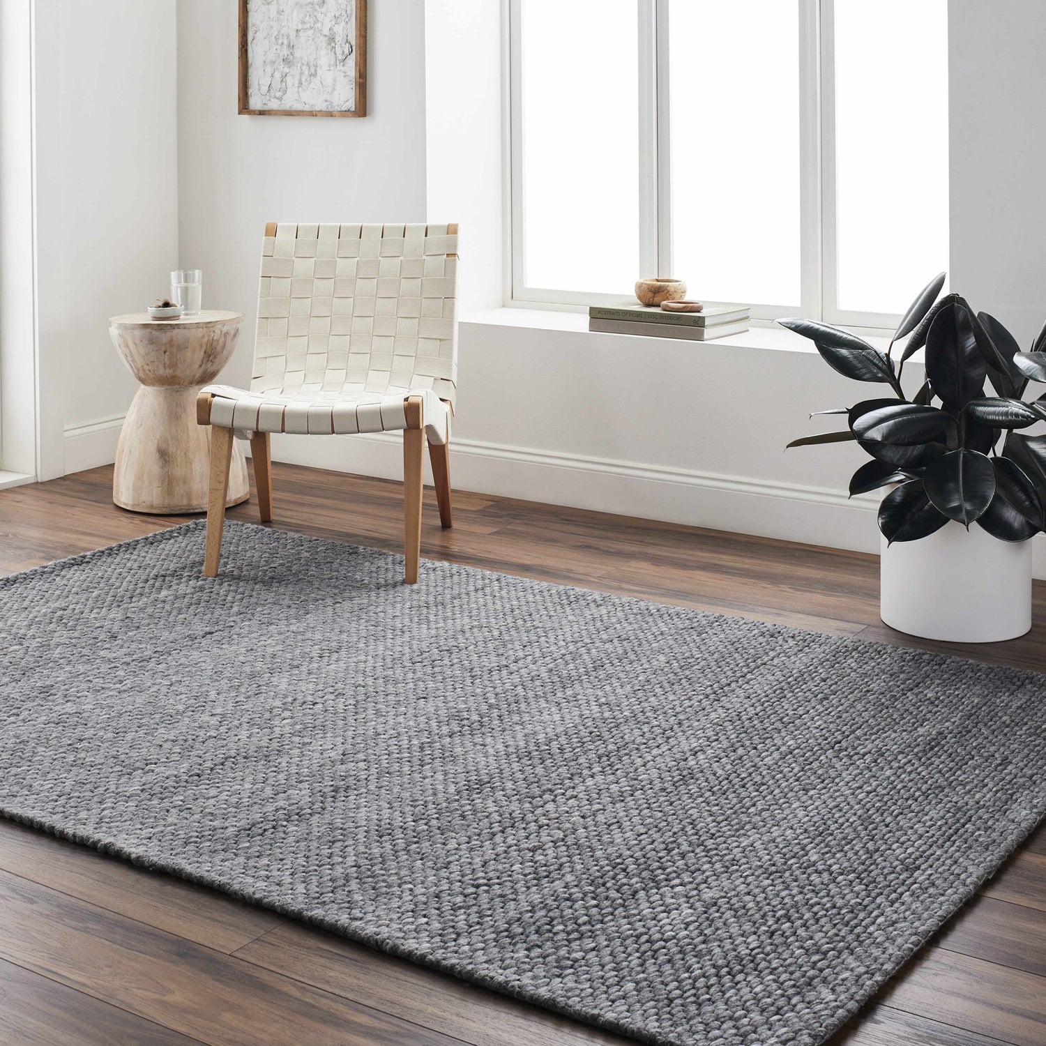 Minimalist living room with gray Ashmont Area Rug, woven chair, wood side table, and dark green plant. Roomscene-Rectangle