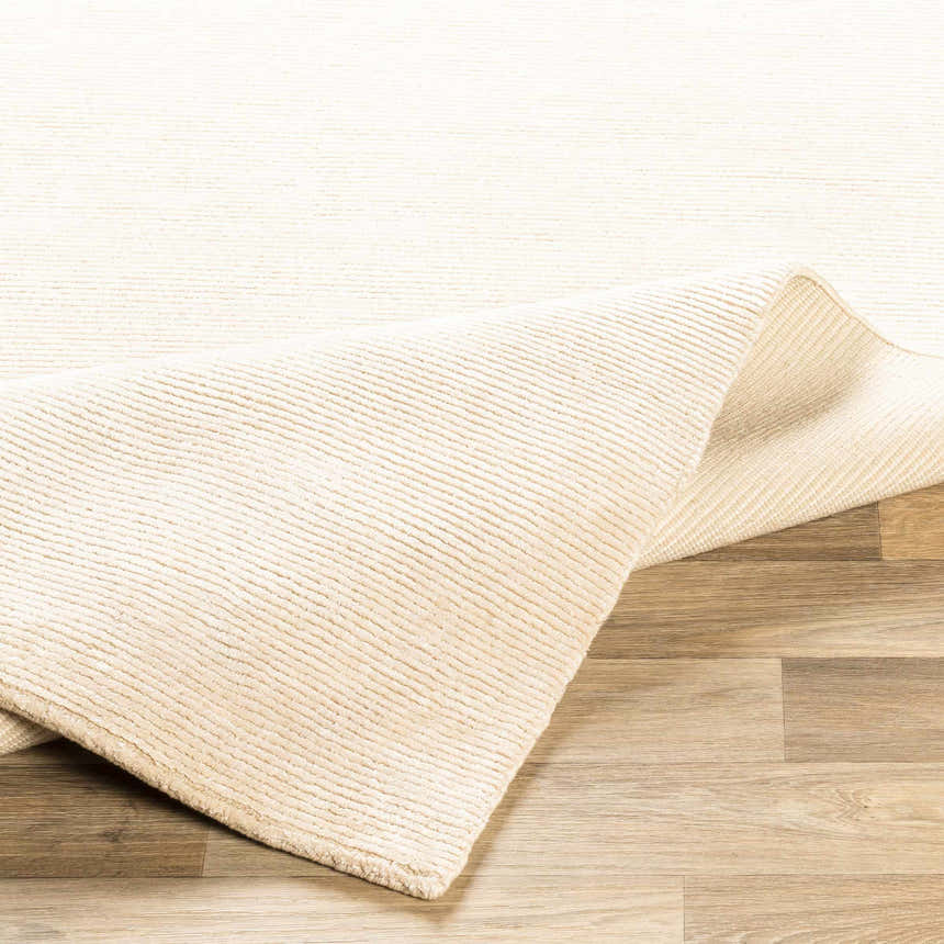 Close-up of the beige Atlas Carpet showing its hand-knotted texture and wool-viscose blend on a wood floor. Fold