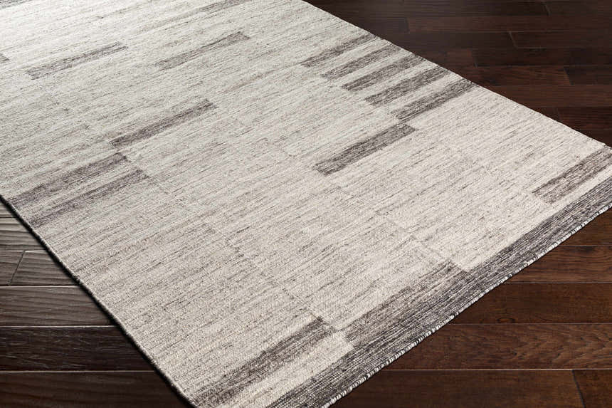 Close-up of the Auchinleck Area Rug showing the cream and charcoal geometric pattern and hand-woven texture on dark wood floors. Corner