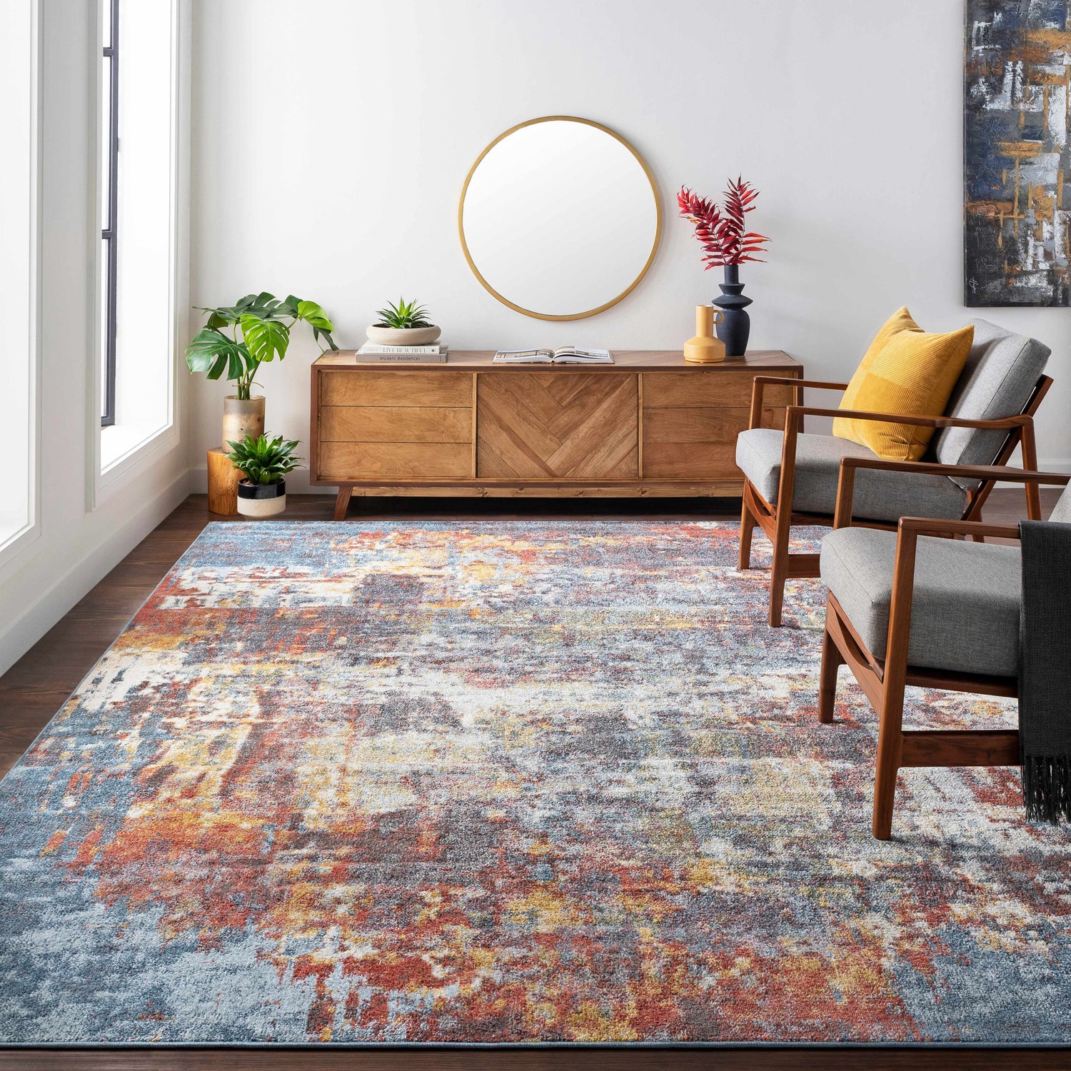 Living room scene with a colorful Auckley abstract area rug, wood furniture, gray chairs, and pops of mustard yellow and brick red. Roomscene-Rectangle