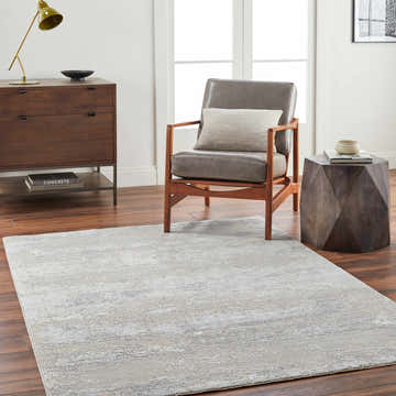 Living room scene with a gray Avani Thick Luxe Boutique Rug, gray chair, wood accents, and dark wood floors. Roomscene-Rectangle