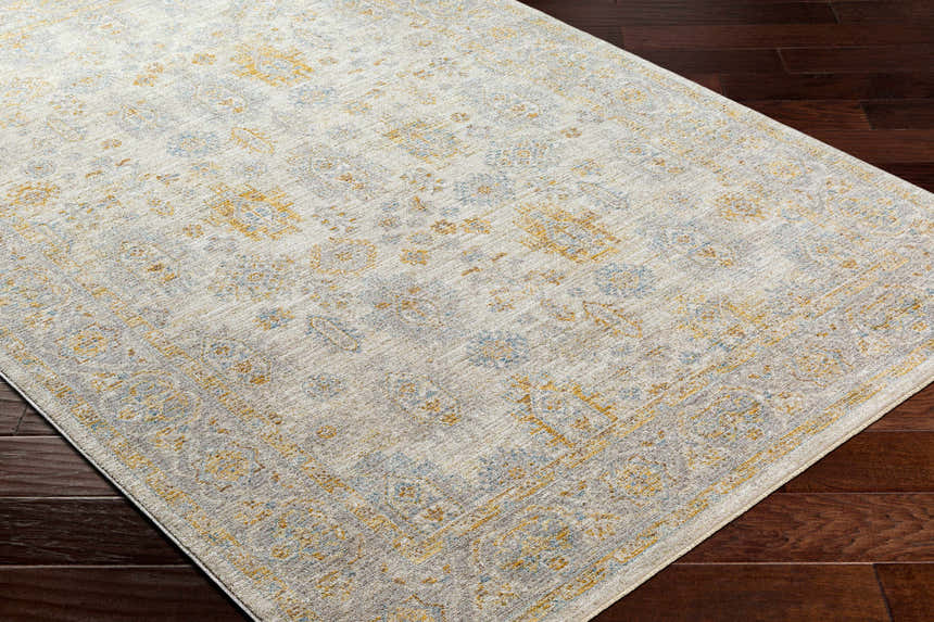 Close-up of the Ayele Thick Luxe Statement Rug on dark wood floors. Features a traditional design in charcoal, mustard, and gray. Corner