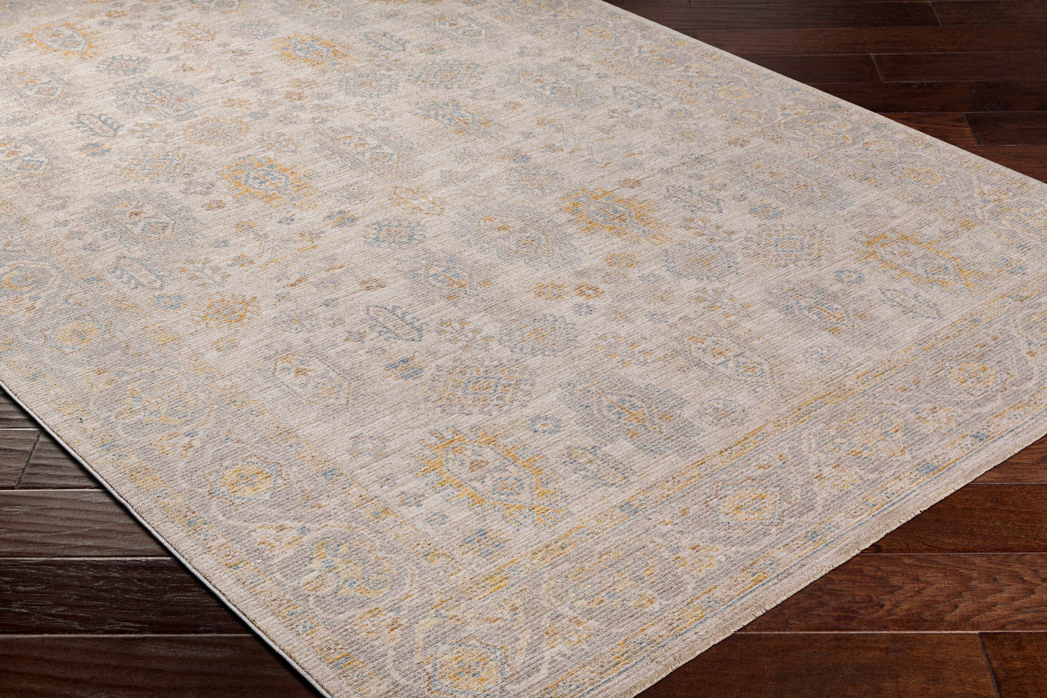 Close-up of the Ayele Thick Luxe Statement Rug in charcoal, gray, mustard, and tan on dark wood flooring. Corner