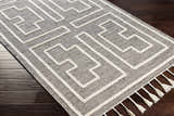 Close-up of the Azra Tasseled Jute & Wool Rug. Charcoal rug with cream geometric pattern and tassels. Hand woven texture. Corner