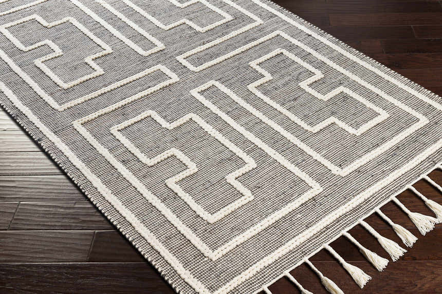 Close-up of the Azra Tasseled Jute & Wool Rug. Charcoal rug with cream geometric pattern and tassels. Hand woven texture. Corner