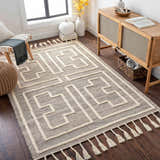 Living room scene with a charcoal and cream Azra Tasseled Jute & Wool Rug, wood floors, and a woven accent chair. Roomscene-Rectangle