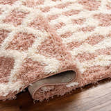 Close-up of the Azura Shag Area Rug. Features a geometric pattern in dark beige, dusty pink, and white thatch colors. Soft texture. Fold
