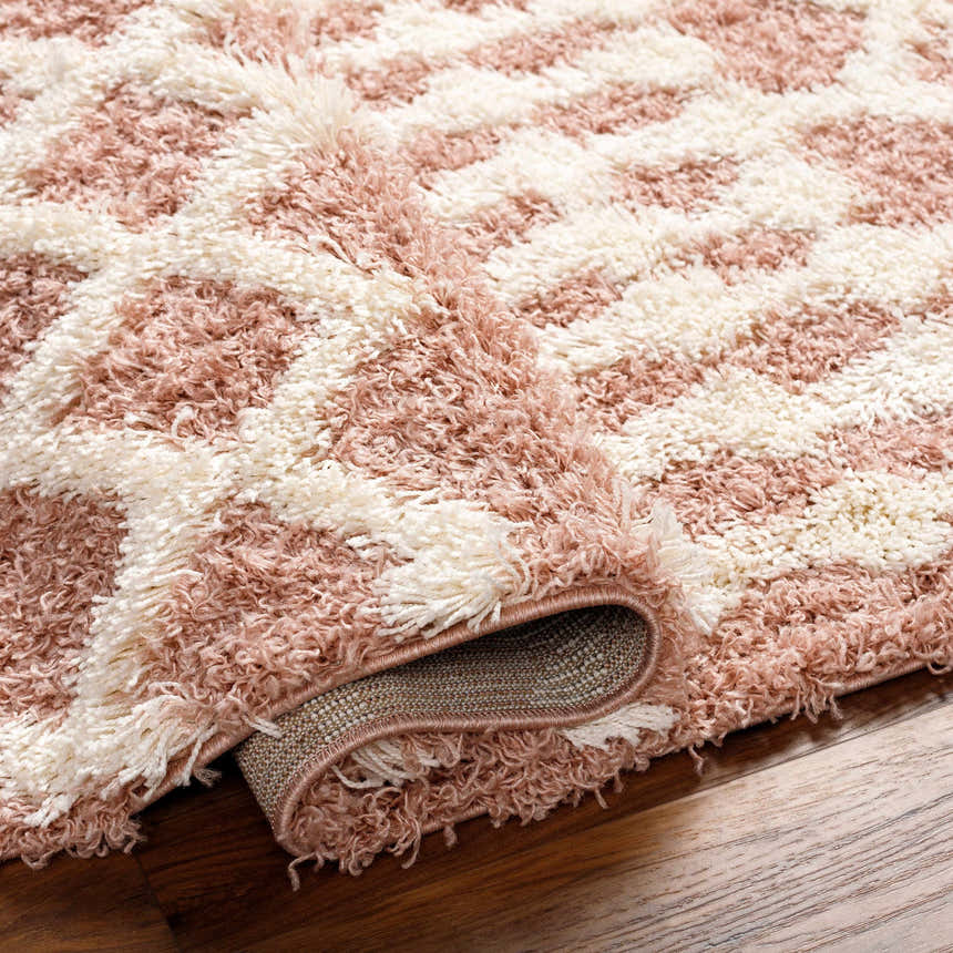 Close-up of the Azura Shag Area Rug. Features a geometric pattern in dark beige, dusty pink, and white thatch colors. Soft texture. Fold