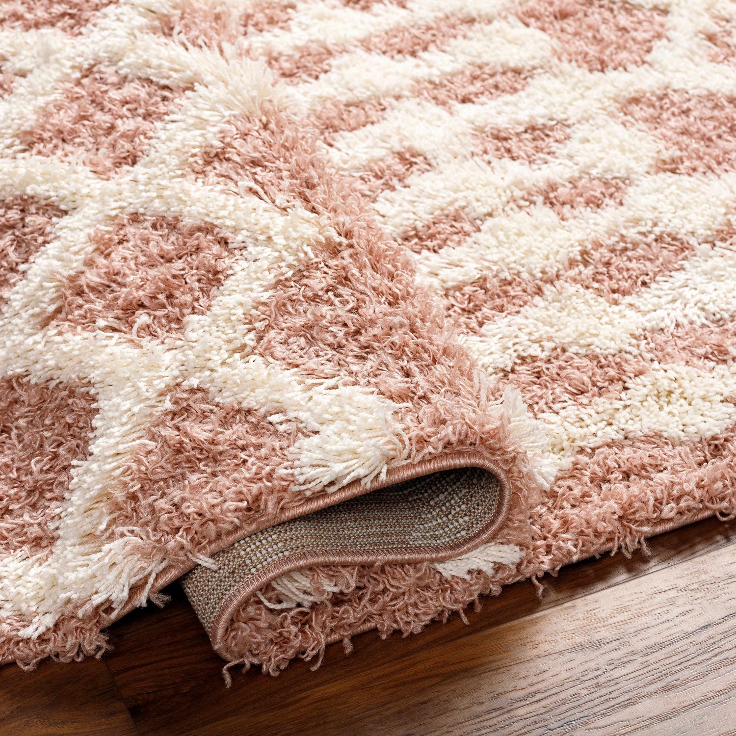 Close-up of the Azura Shag Area Rug. Features a geometric pattern in dark beige, dusty pink, and white thatch colors. Soft texture. Fold