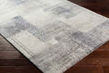 Close-up of the Bacca Area Rug showing its gray, light gray, and nutmeg contemporary pattern and machine woven texture. Corner