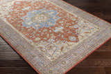 Bacoor Washable Area Rug on dark wood floor. Traditional oriental rug with brick red, beige, and blue floral pattern. Corner