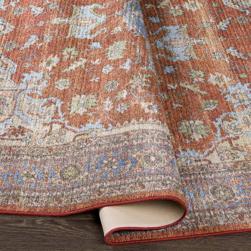 Close-up of the Bacoor Washable Area Rug showing its brick red, beige, and blue traditional pattern and woven texture. Fold