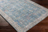 Close-up of the blue, cream, and rose Bagontapay Washable Area Rug with a traditional floral pattern on dark wood floors. Corner
