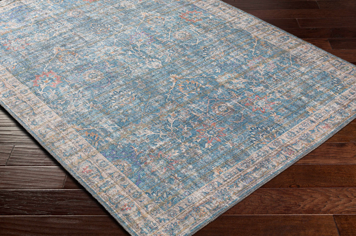 Close-up of the blue, cream, and rose Bagontapay Washable Area Rug with a traditional floral pattern on dark wood floors. Corner