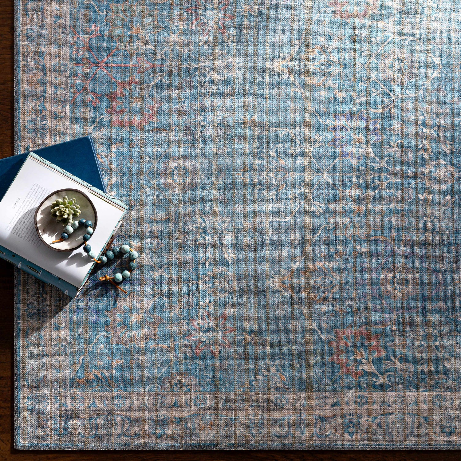 Close-up of the blue and cream Bagontapay Washable Area Rug with traditional floral pattern and books. Styleshot
