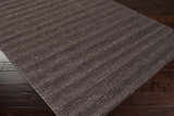 Close up of the hand-loomed Banbury Area Rug, a black wool rug with subtle stripes on dark wood flooring. Corner