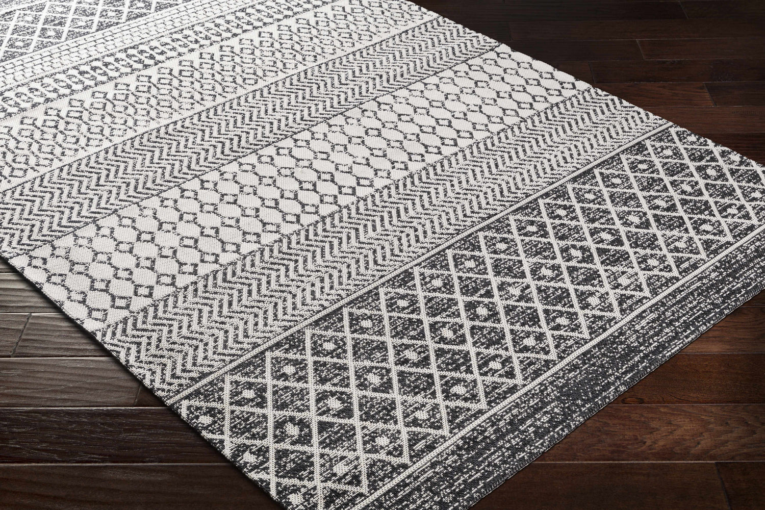 Close-up of Barnwood Washable Area Rug. Black and cream cotton rug with geometric, bohemian-inspired pattern on dark wood floor. Corner