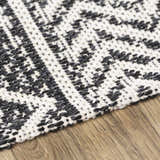 Close-up of the Barnwood Washable Area Rug. Black and cream woven cotton rug with a geometric pattern on a wood floor. Texture