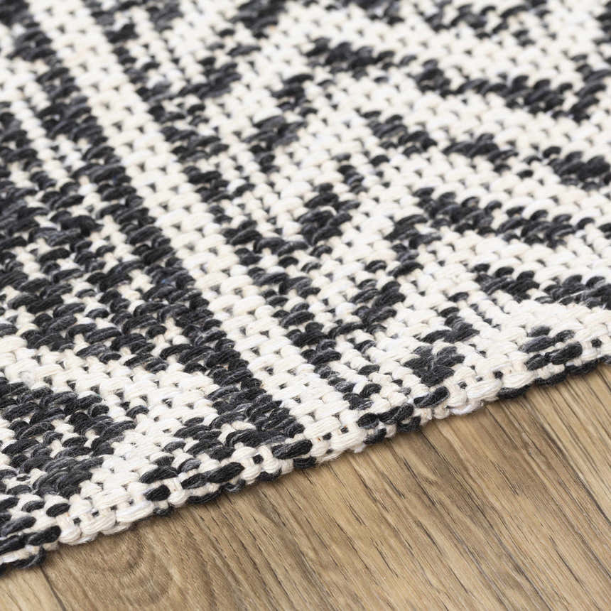 Close-up of the Barnwood Washable Area Rug. Black and cream woven cotton rug with a geometric pattern on a wood floor. Texture