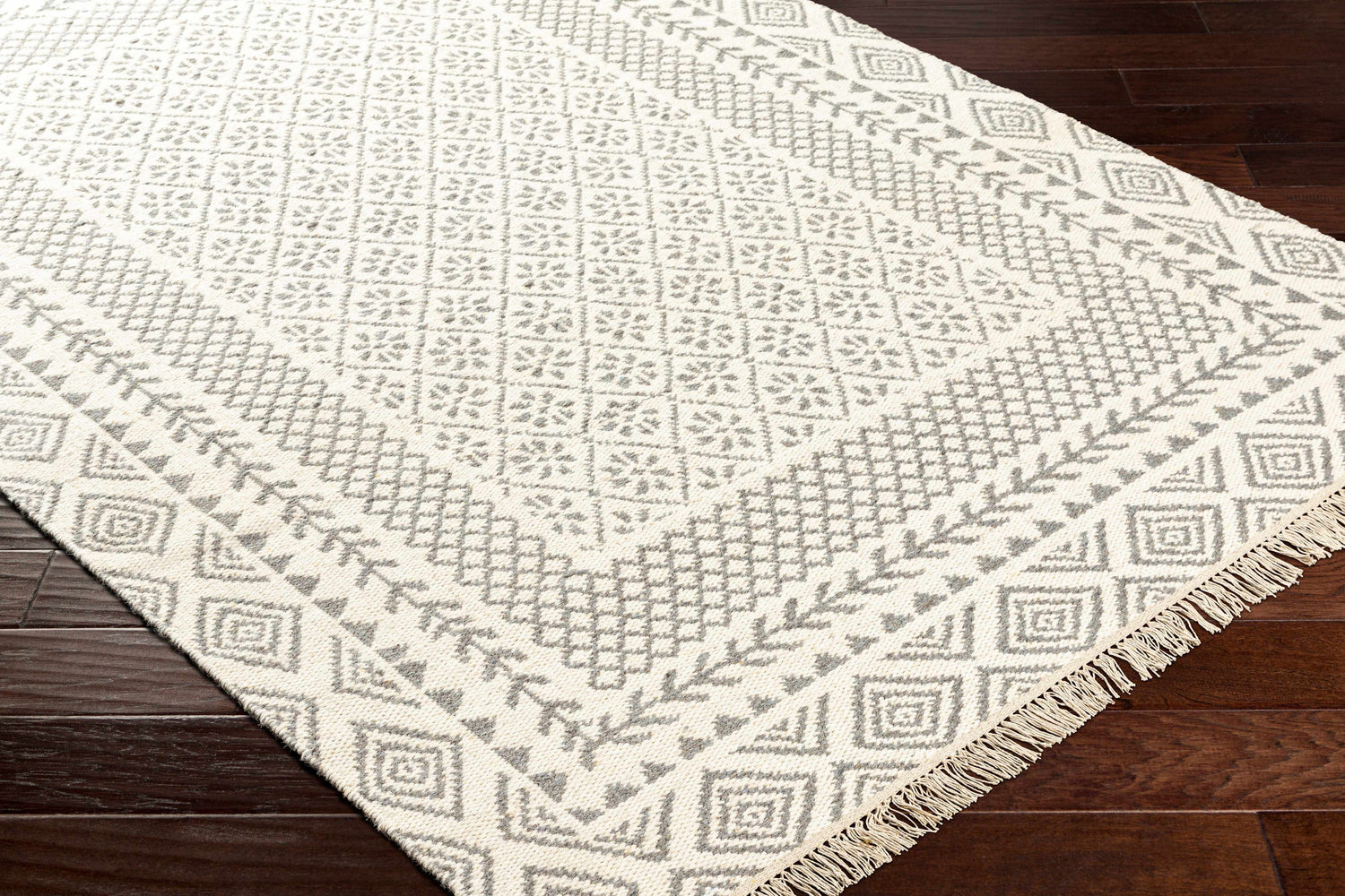 Close-up of the Bayou Area Rug, a hand-woven wool rug in beige and gray with a geometric pattern and fringe. Corner