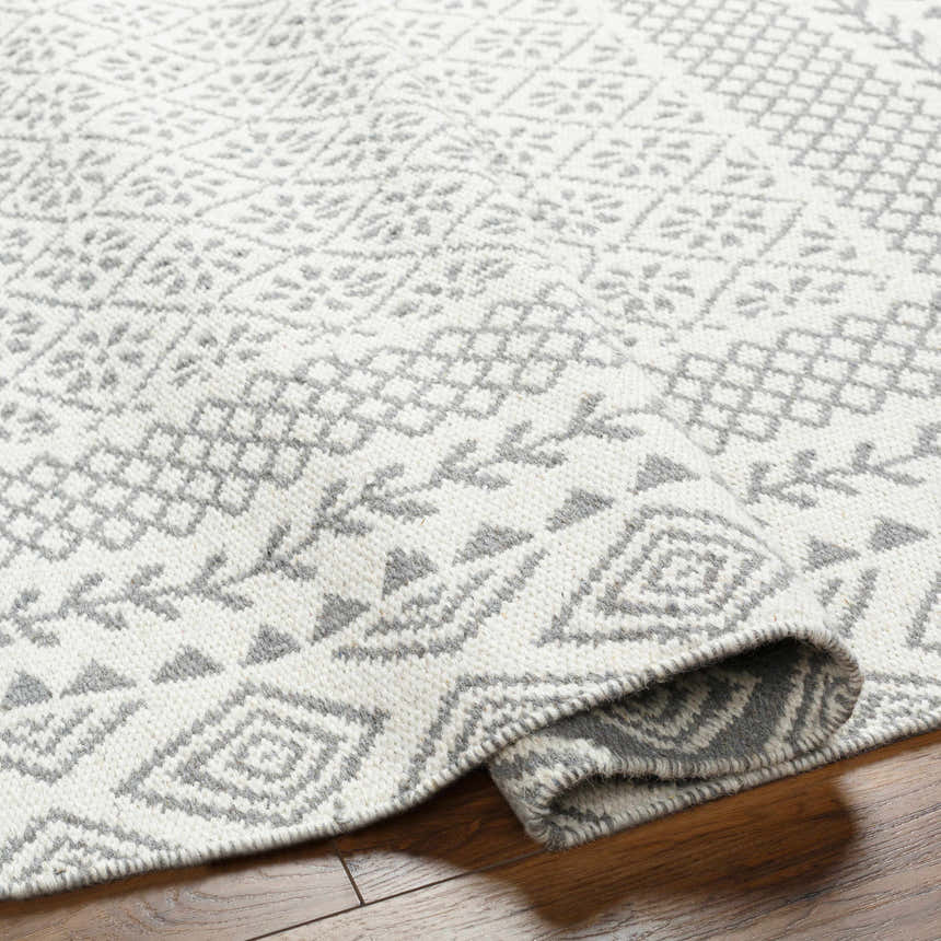 Close-up of the Bayou Area Rug showing its hand-woven texture and beige and gray geometric pattern on a wood floor. Fold