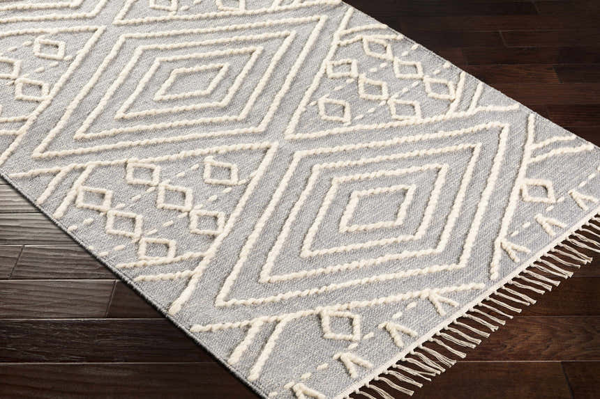 Close-up of the hand-woven Bealeton Area Rug. Cream geometric pattern on slate gray cotton with fringe detail. Corner