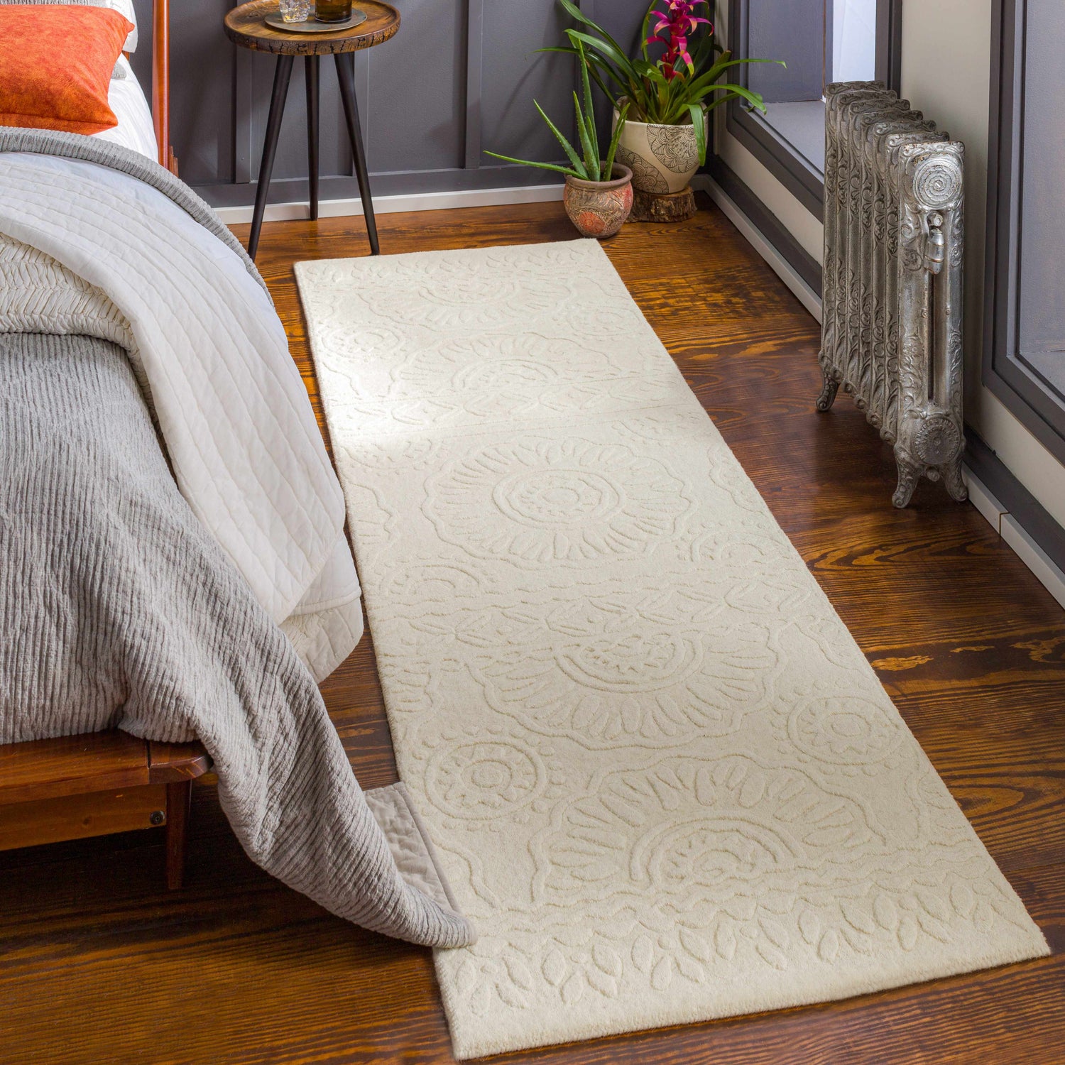 Bedroom scene with beige Beighton Clearance Rug runner on wood floor. Bed, plants, and radiator complete the cozy room. Roomscene-Runner