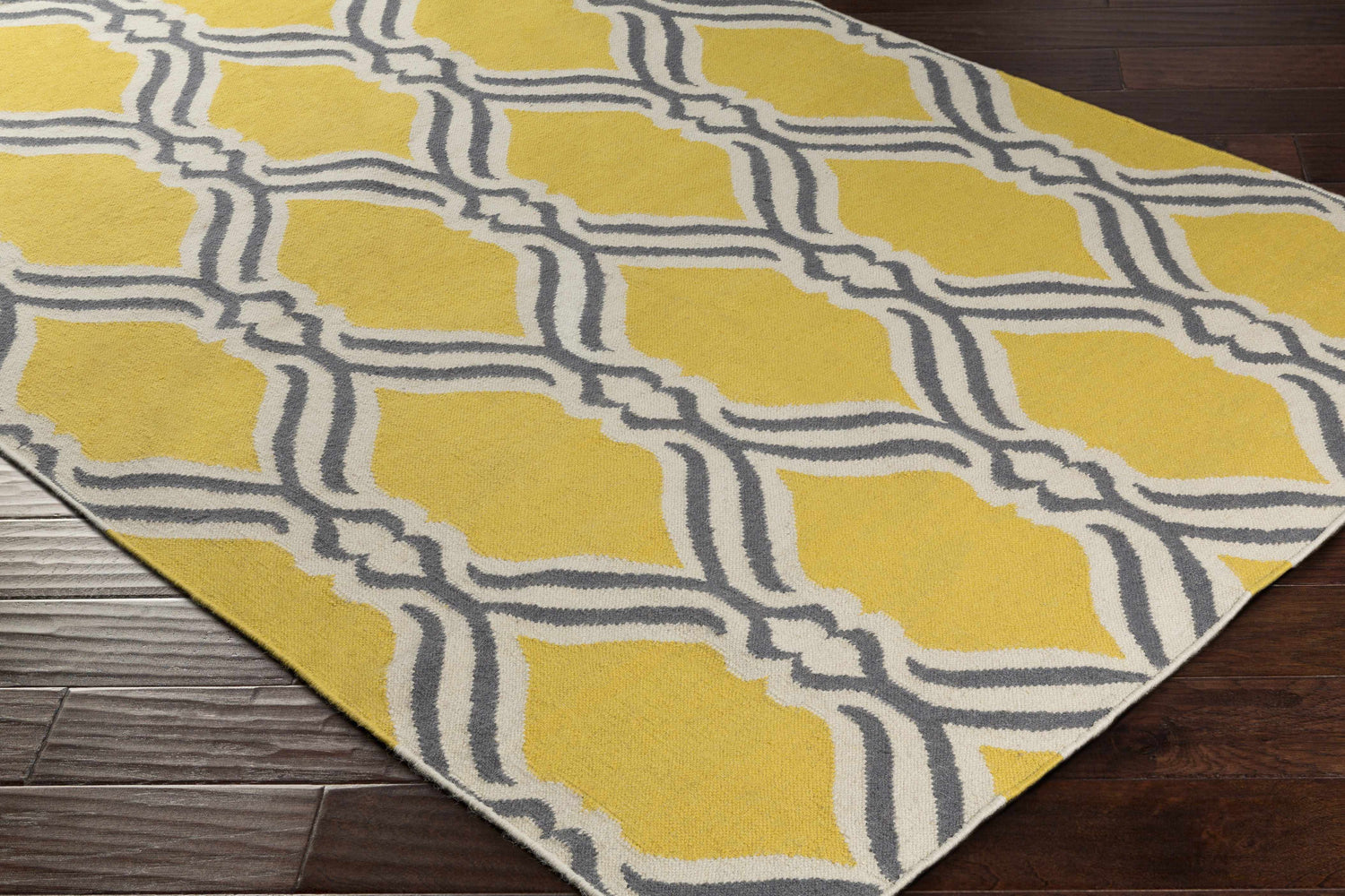 Close-up of the Bells Area Carpet. Hand-woven wool rug with a yellow, gray, and cream geometric trellis pattern. Corner