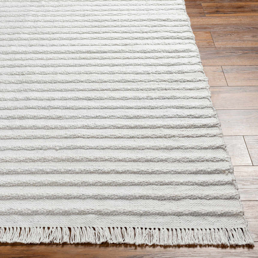 Close-up of light gray Benek Area Rug showing hand woven texture, geometric pattern, and fringe detail on wood floor. Front
