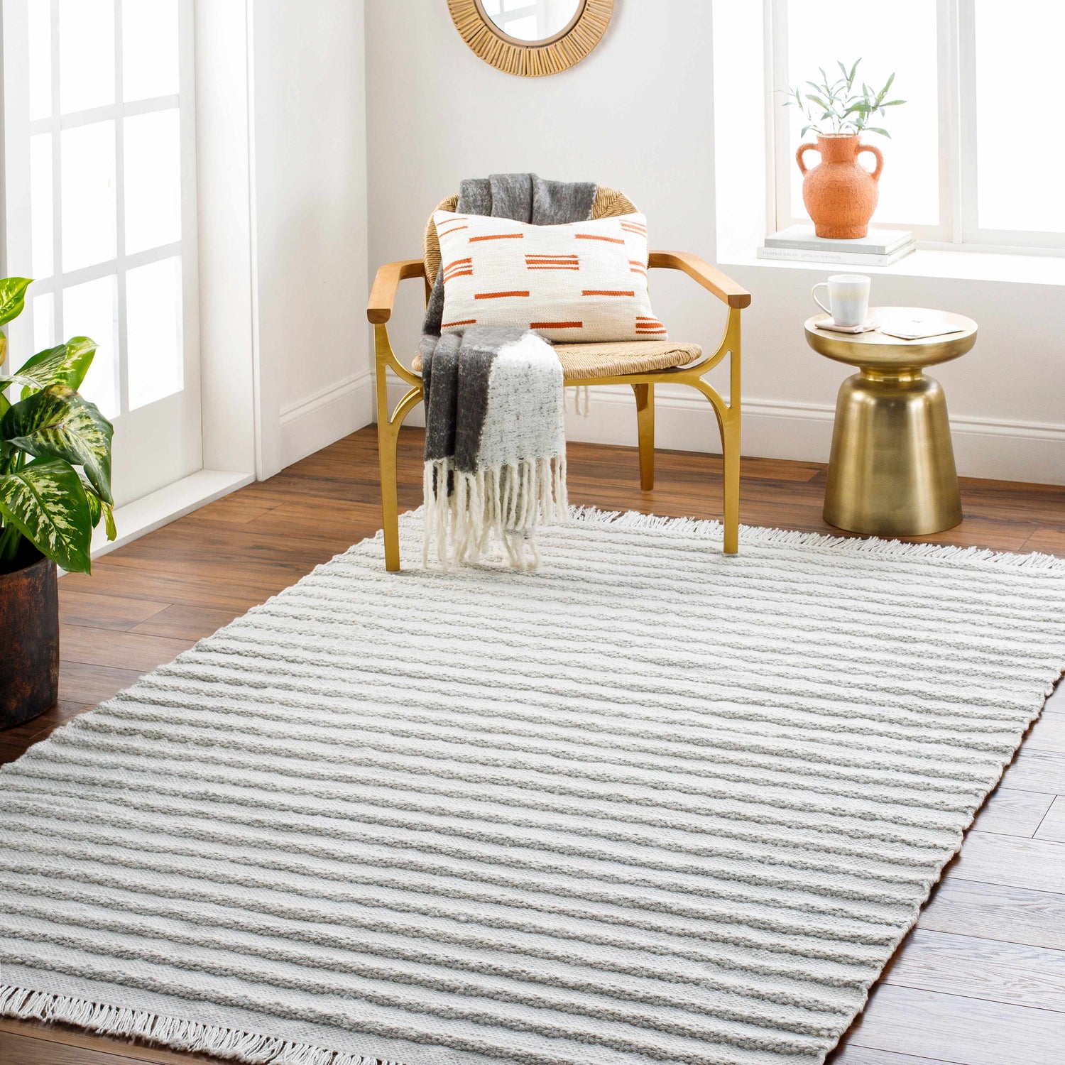 Light gray Benek Area Rug in a bright, modern living room with wood floors, gold side table, and woven chair. Roomscene-Rectangle