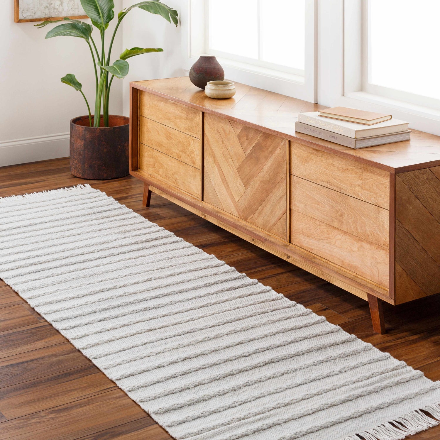 Entryway scene with a light gray Benek Area Rug runner, wooden cabinet, plant, and books. Roomscene-Runner